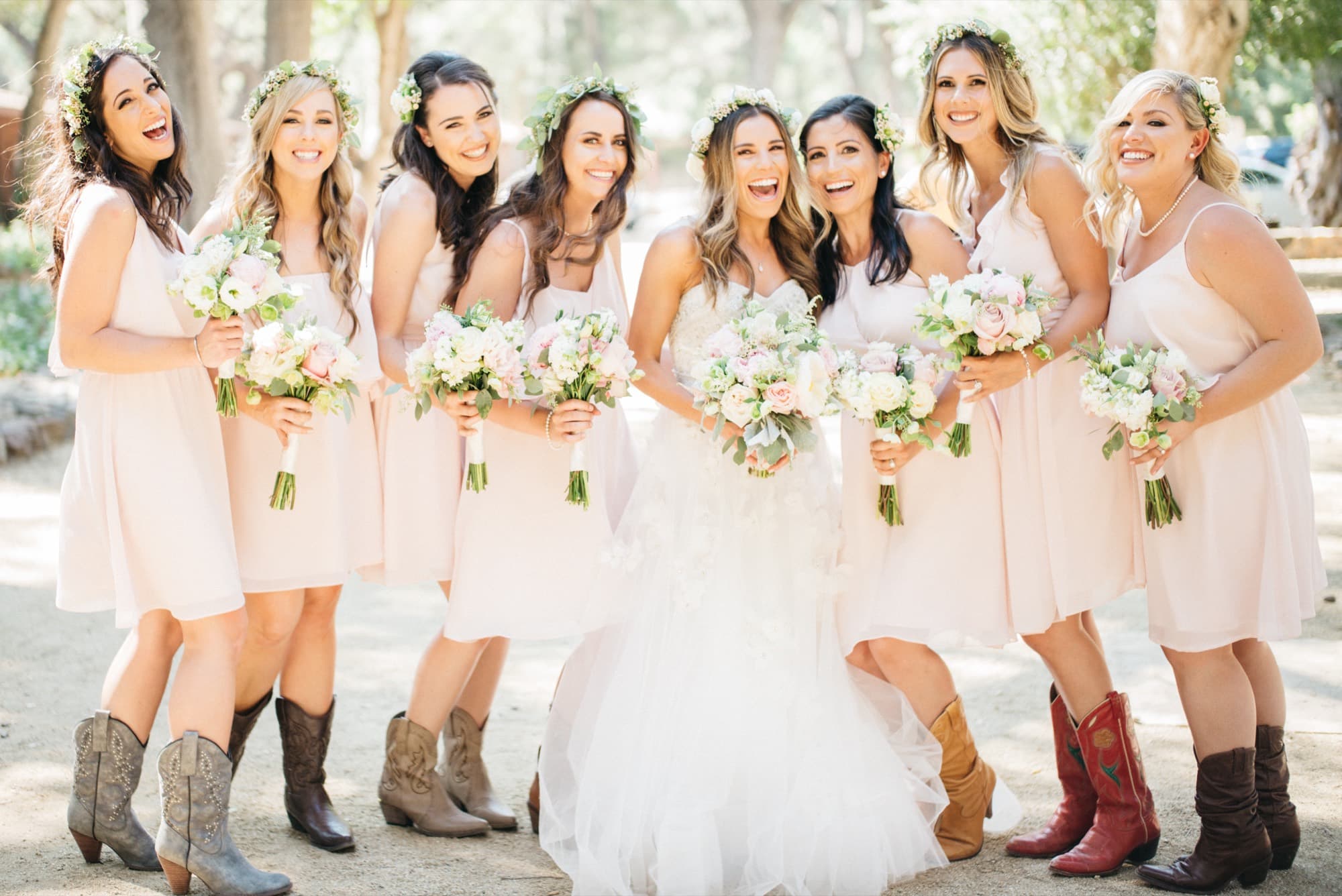 Bridal party in blush dresses and cowboy boots laughing outdoors