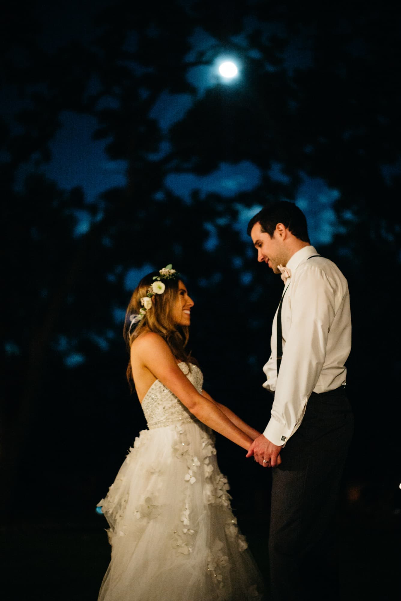 Bride and groom holding hands under a full moon at night