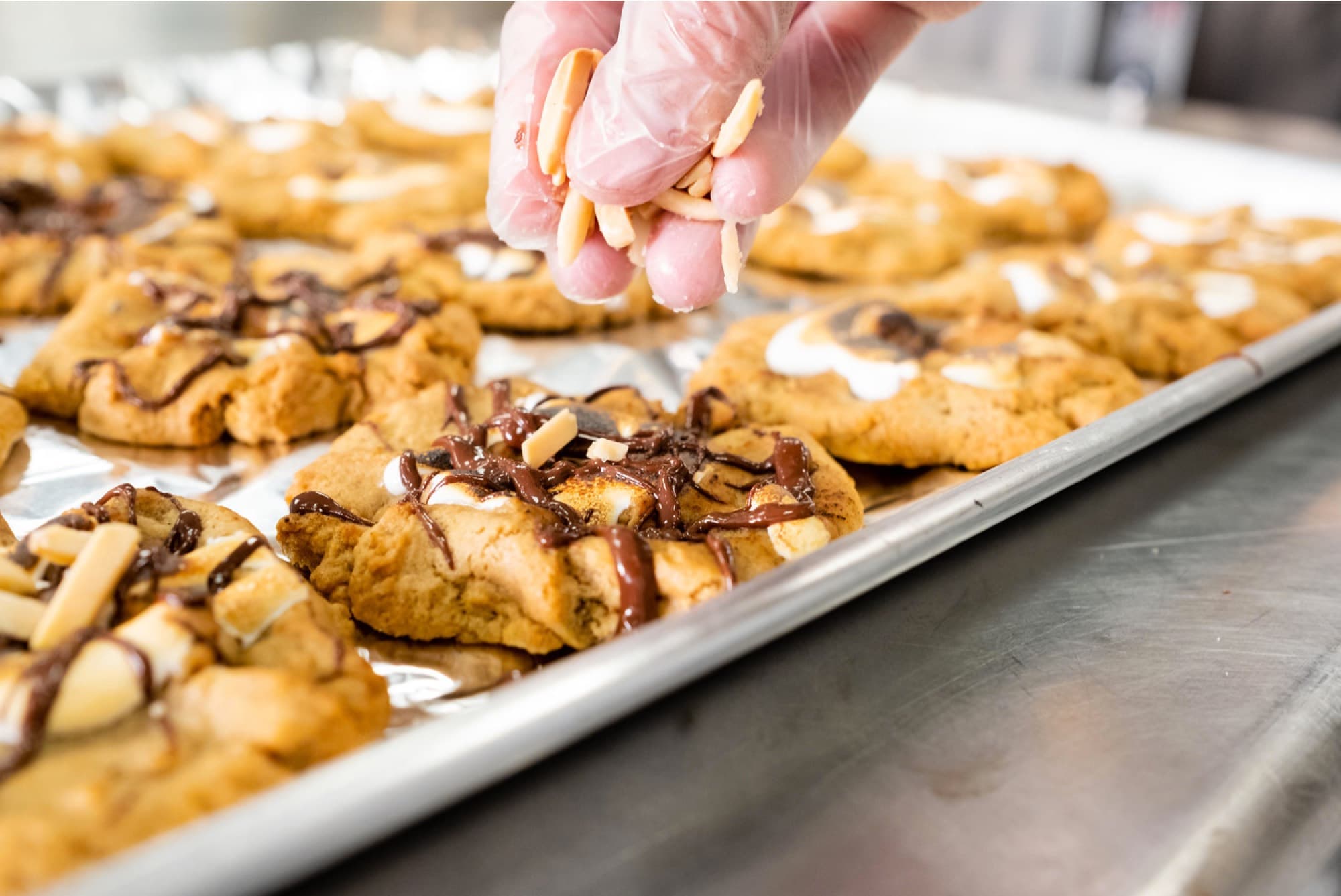 Baker adding almond slivers to trays of fresh Chunk-N-Chip cookies