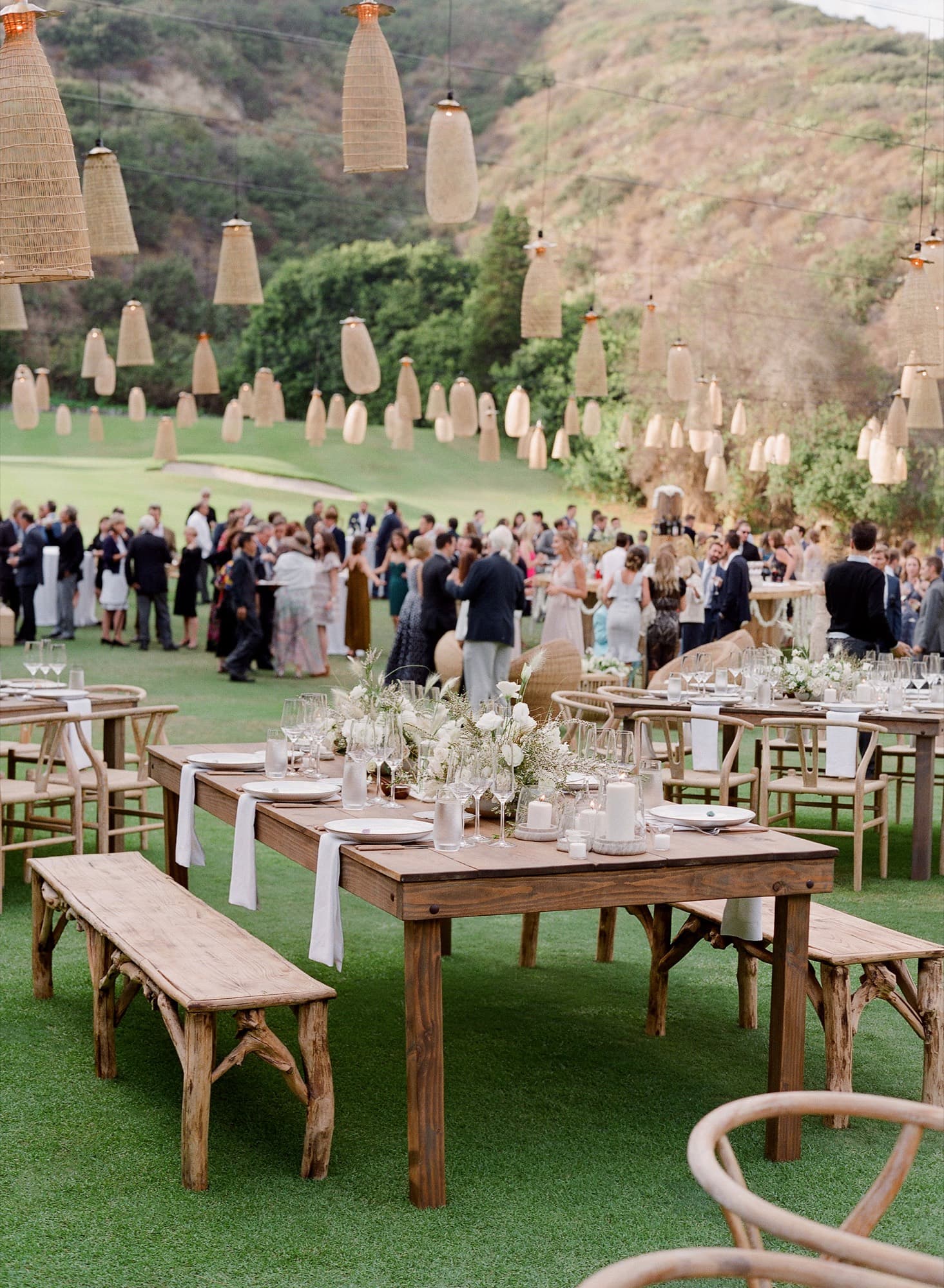 Outdoor wedding reception with wooden farm tables and hanging lanterns