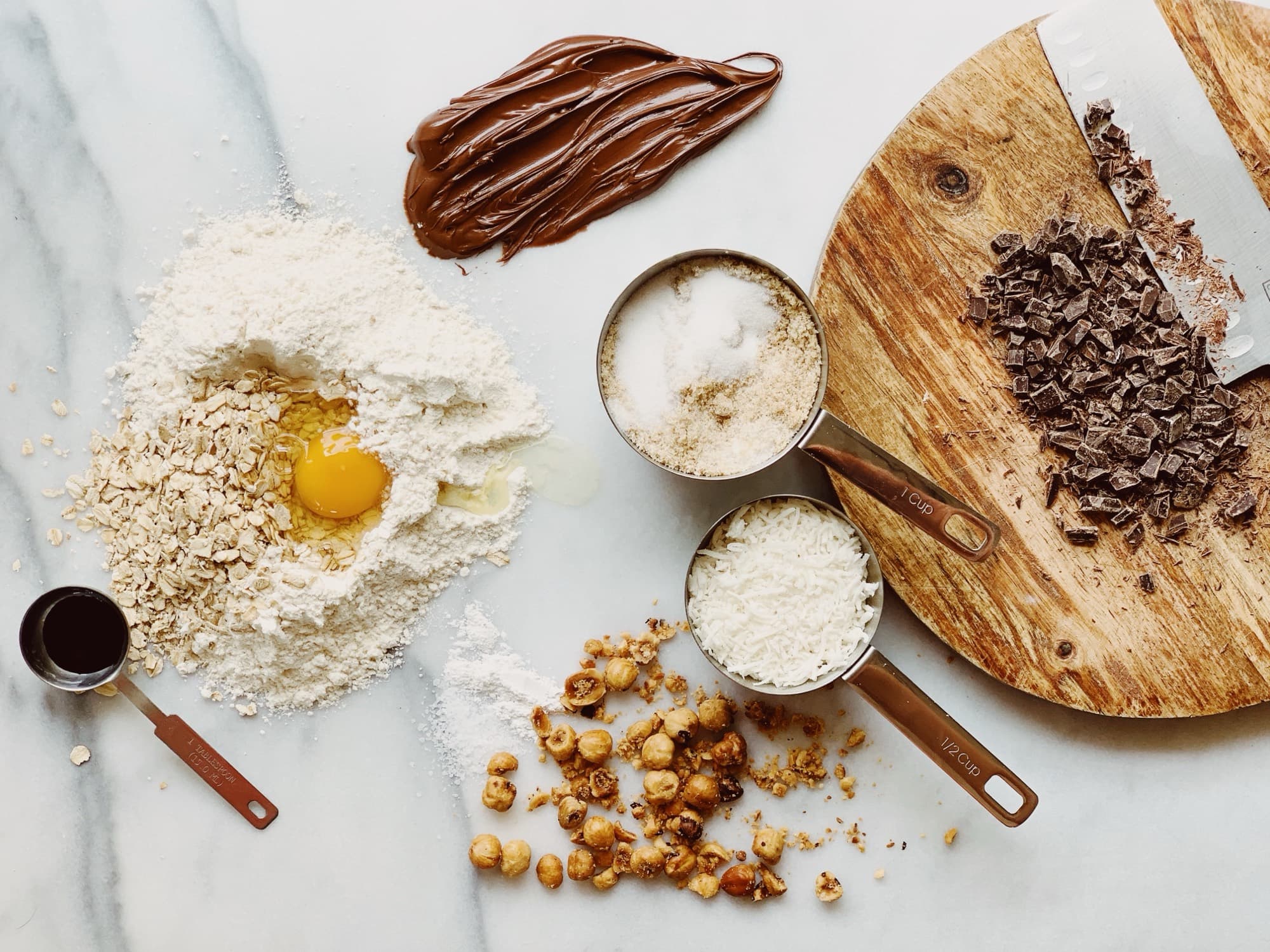Flour, eggs, chocolate, and toffee laid out on marble for small-batch cookie baking