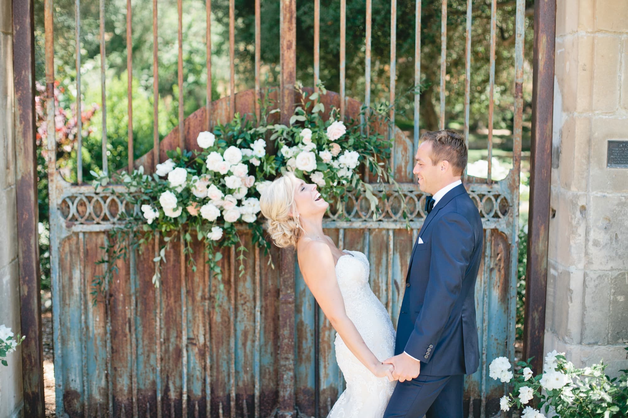 Bride and groom beside a rustic garden gate decorated with white roses